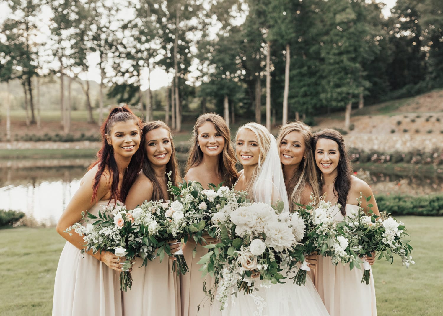 Bride and bridesmaids pose with flowers in front of water
