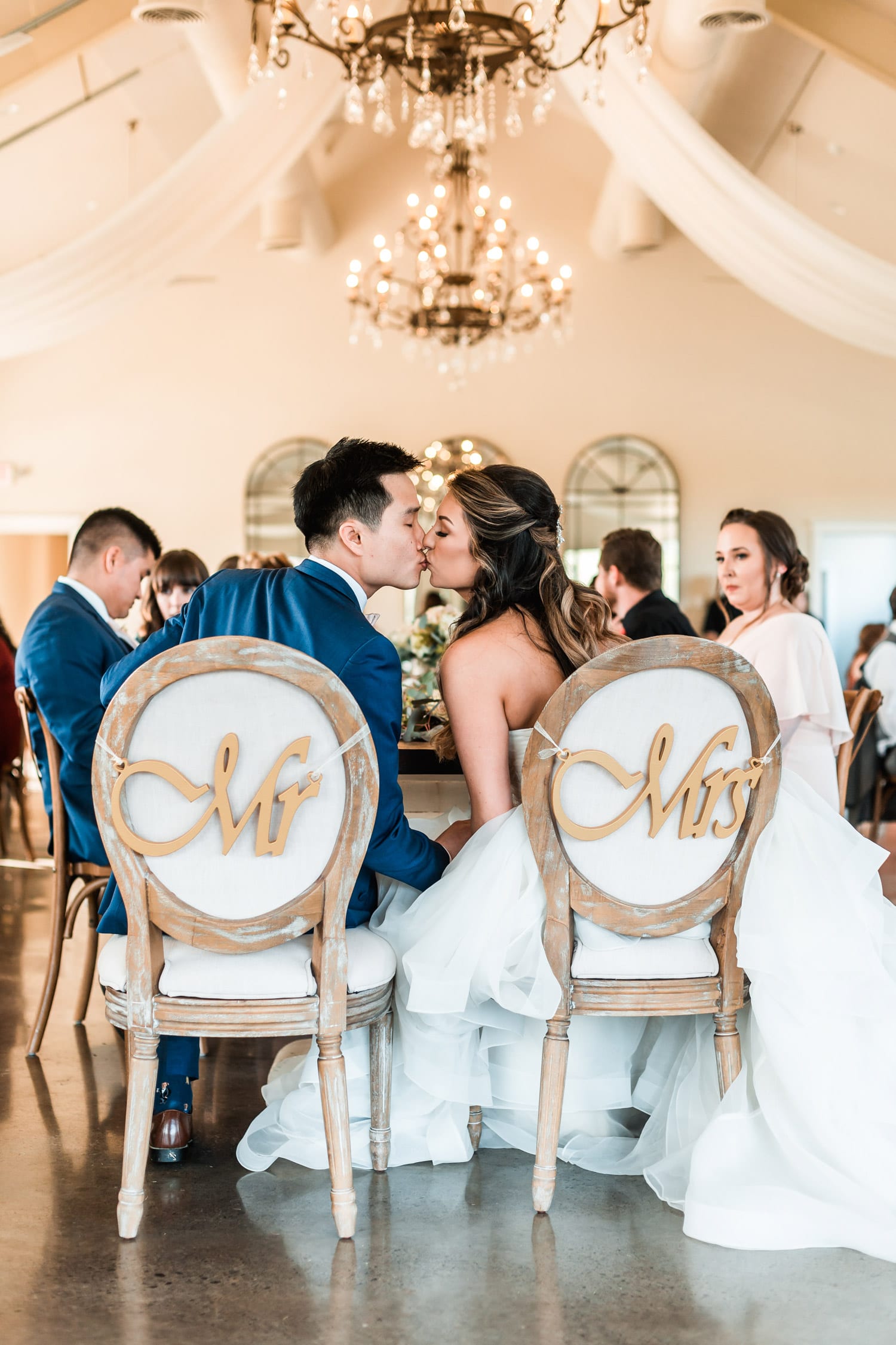 Bride and groom kiss in Mr. and Mrs. chairs