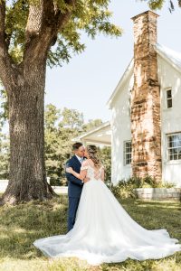 Bride and groom kissing next to a tree and white house at a north Georgia wedding venue