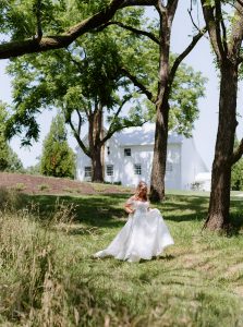 Bride walks down a grassy hill in the woods in front of a white house at a north Georgia wedding venue