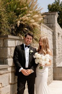 Bride holds groom and flowers while standing next to a grey brick wall at a north Georgia wedding venue