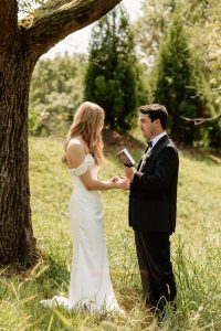 Groom reads vows to bride in front tree and grassy hills at a a north Georgia wedding venue