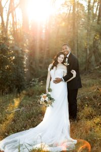 Bride and groom holding each other while posing in the forest with a sunset behind them at a north Georgia wedding venue
