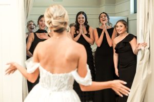 Bride reveals wedding dress to happy bridesmaids in bridal suite at The Greystone Estate wedding venue