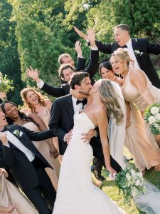 Groom leans bride back and kisses her as wedding party celebrates behind them at a North Georgia wedding venue