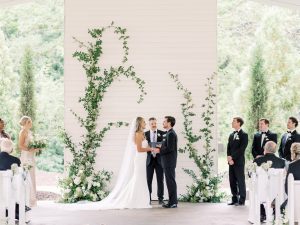 Bride and groom exchange vows inside a white outdoor chapel at a North Georiga wedding venue as the wedding party looks toward them