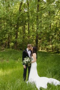 Bride and Groom holding flowers while kissing in the woods at a north Georgia wedding venue